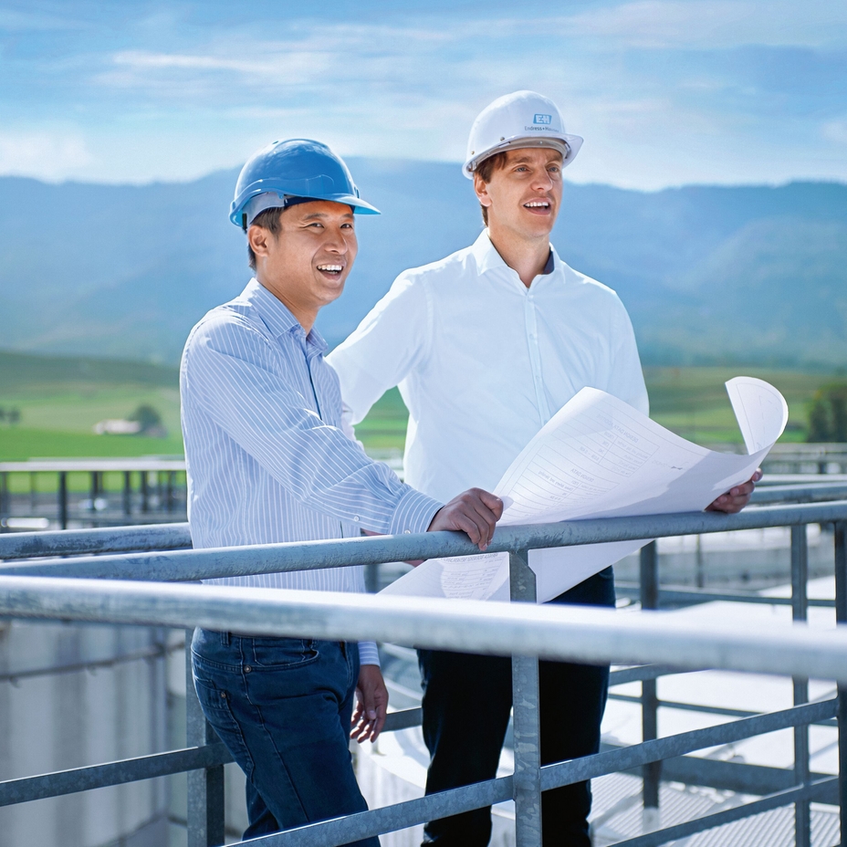 Two engineers standing on top of a storage tank in front of green landscape.